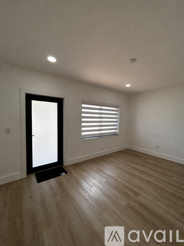 A room with wooden flooring and a black door leading to another room.