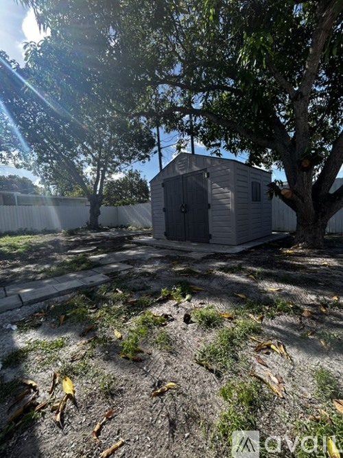 A small building sits in a yard with a tree in front of it.