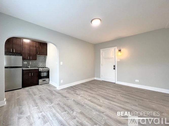 A spacious room with a kitchenette and a door leading to another room.