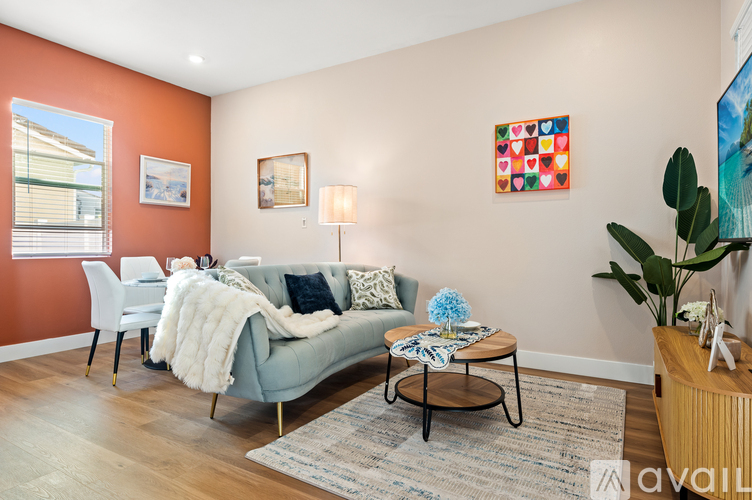 A living room with a grey couch, a white chair, a small table with a blue flower, a lamp, a painting, a potted plant and a rug.