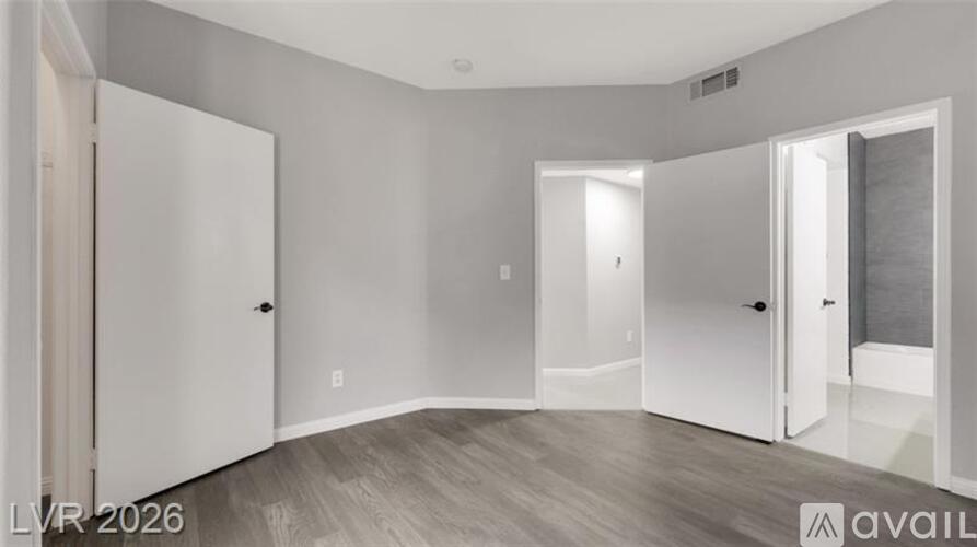 A room with white walls and a wooden floor with a door on the left and a window on the right.