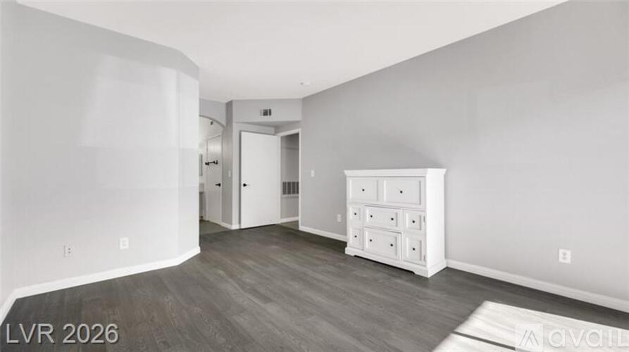 A spacious room with a white dresser and a wooden floor.