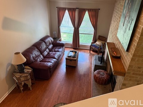 A brown leather couch sits in a living room with a window and a lamp.