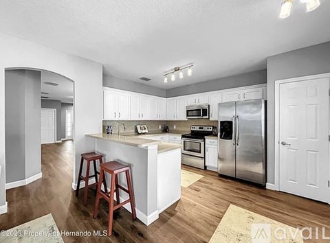 A kitchen with white cabinets and a white island with a refrigerator, microwave, and oven.