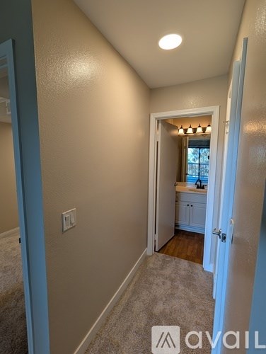 A hallway with a carpeted floor and a doorway leading to a kitchen.