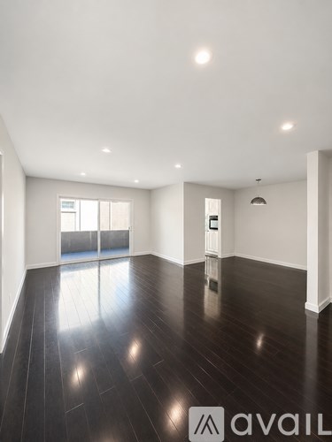 A spacious room with dark wood flooring and white walls.