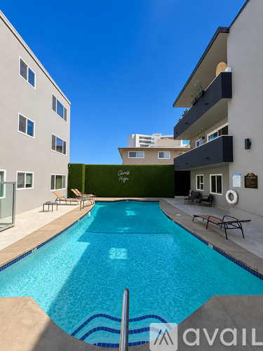 A swimming pool in front of a building with a green wall and lounge chairs.