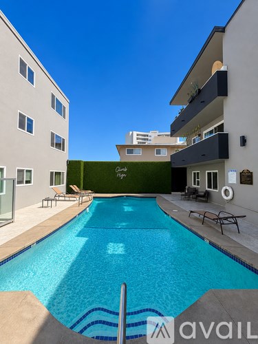 A swimming pool in front of a building with a green wall and lounge chairs.