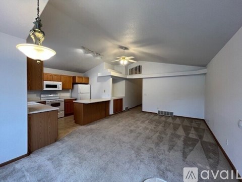 A living room with a grey carpet and a kitchen area in the background.