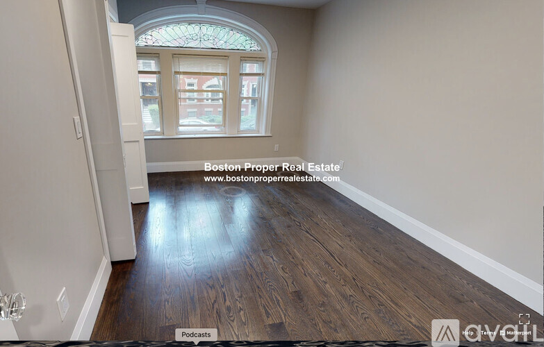 A room with wooden flooring and a window with a view of a building outside.