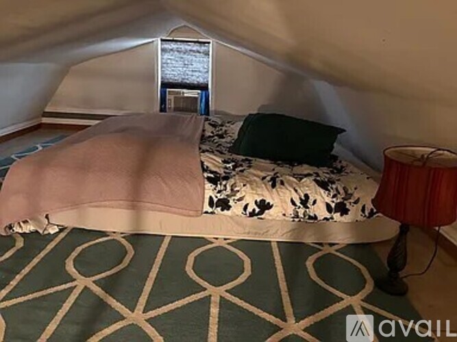 A bed with a pink blanket and a black and white patterned pillow is in a room with a patterned carpet.