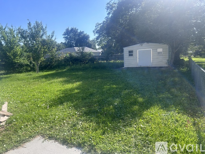 A white shed sits in a grassy field with trees in the background.