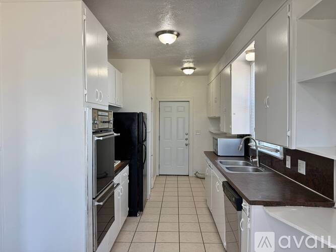 A kitchen with white cabinets and appliances, a black refrigerator, and a white door.