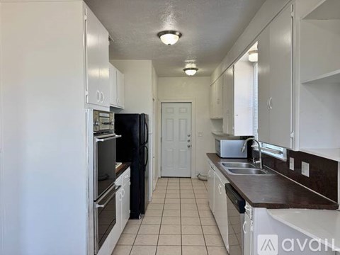 A kitchen with white cabinets and appliances, a black refrigerator, and a white door.