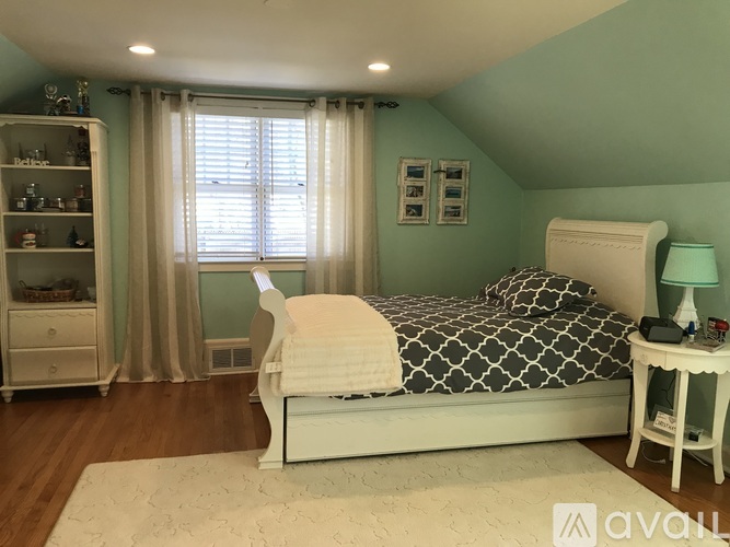 A bedroom with a white bed and a white nightstand with a lamp on it.