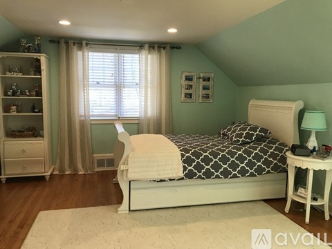 A bedroom with a white bed and a white nightstand with a lamp on it.