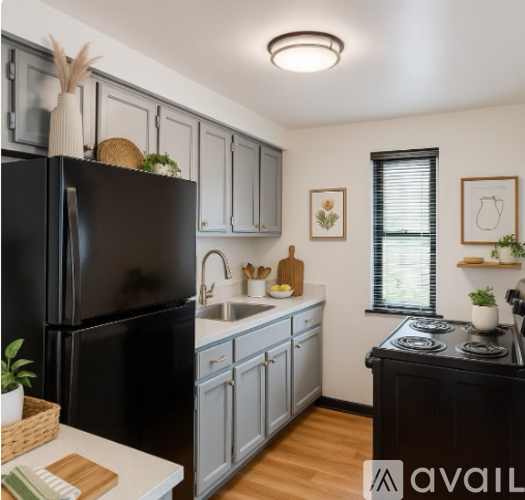 A black refrigerator stands in a kitchen with wooden floors and white walls.
