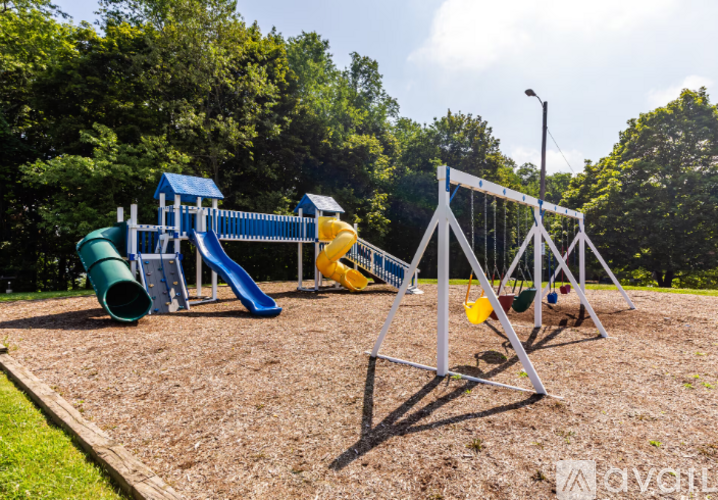 A playground with a blue and yellow slide, a green tunnel, and a white swing set.