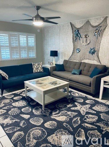 A living room with a blue couch, a white coffee table, and a rug with shell patterns.