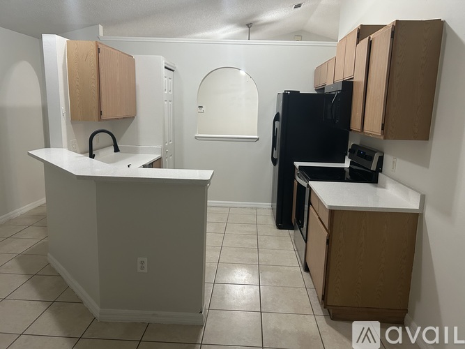 A kitchen with a black refrigerator, white countertops, and wooden cabinets.