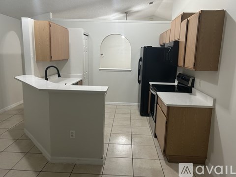 A kitchen with a black refrigerator, white countertops, and wooden cabinets.
