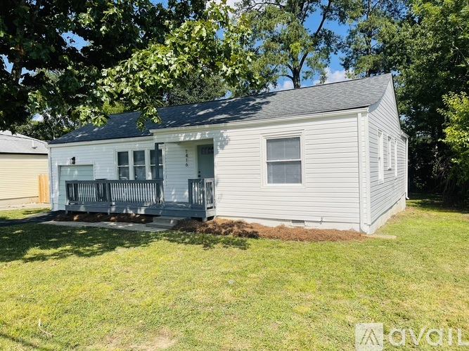 A house with a grey siding and a black roof is surrounded by green grass and trees.