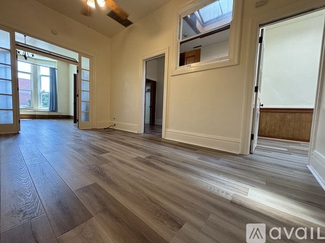 A spacious room with wooden flooring and a large window.