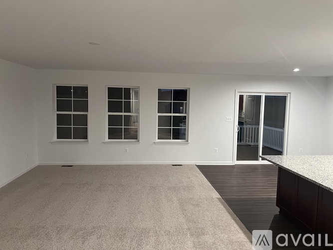 A spacious room with a carpeted floor, three windows, and a door leading to a balcony.