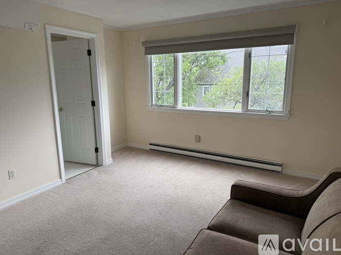 A room with a brown couch, a window with a view of trees, and a door leading to another room.