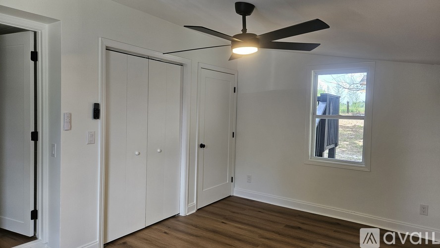A room with a ceiling fan and a window with a view of a fence and trees.