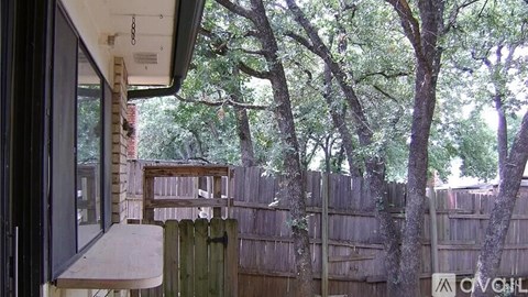 A patio with a table and chairs overlooks a backyard with a fence and trees.