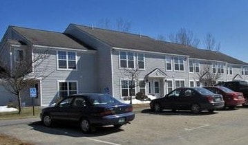 A black car is parked in a parking lot in front of a building.