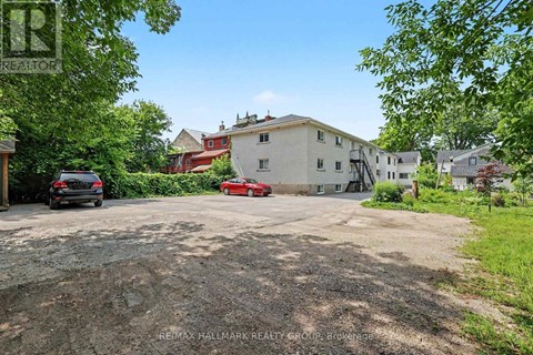 A gravel driveway leads to a white house with a red car parked in front.
