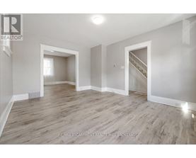 A spacious room with wooden flooring and white walls, featuring a staircase with a railing.