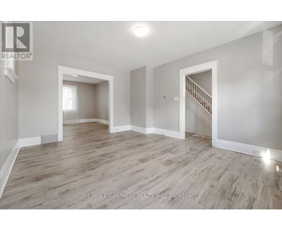A spacious room with wooden flooring and white walls, featuring a staircase with a railing.