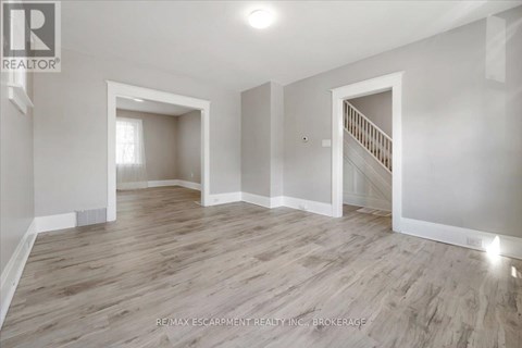 A spacious room with wooden flooring and white walls, featuring a staircase with a railing.