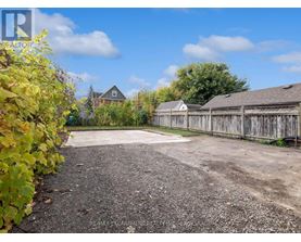 A gravel driveway leads to a wooden fence and a house.