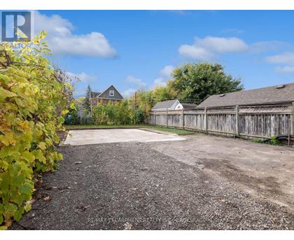 A gravel driveway leads to a wooden fence and a house.