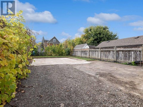 A gravel driveway leads to a wooden fence and a house.