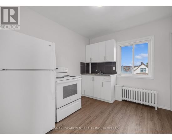 A white refrigerator is in a kitchen with wood floors and white walls.