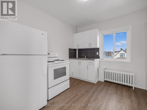 A white refrigerator is in a kitchen with wood floors and white walls.