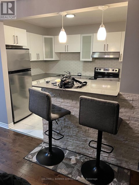 A kitchen with a refrigerator, stove, and bar stools.