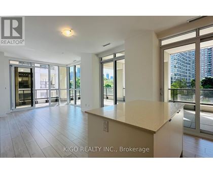 A spacious room with a large island in the middle and sliding glass doors leading to a balcony.