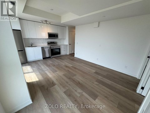 A spacious room with wooden flooring and white walls, featuring a kitchen area with a microwave and oven.