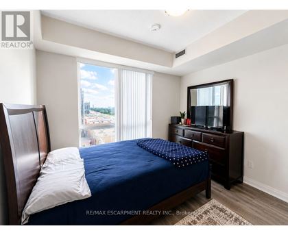 A bedroom with a bed, dresser, and window overlooking a parking lot.