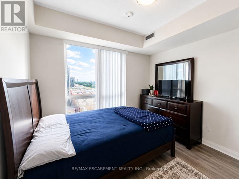 A bedroom with a bed, dresser, and window overlooking a parking lot.
