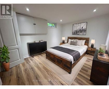 A bedroom with a bed, nightstand, and a plant.