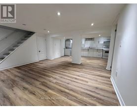 A spacious room with wooden flooring and a staircase on the left side.
