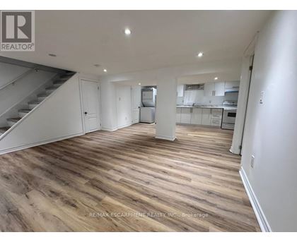 A spacious room with wooden flooring and a staircase on the left side.