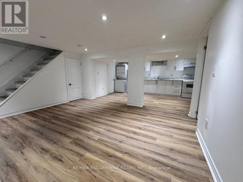 A spacious room with wooden flooring and a staircase on the left side.
